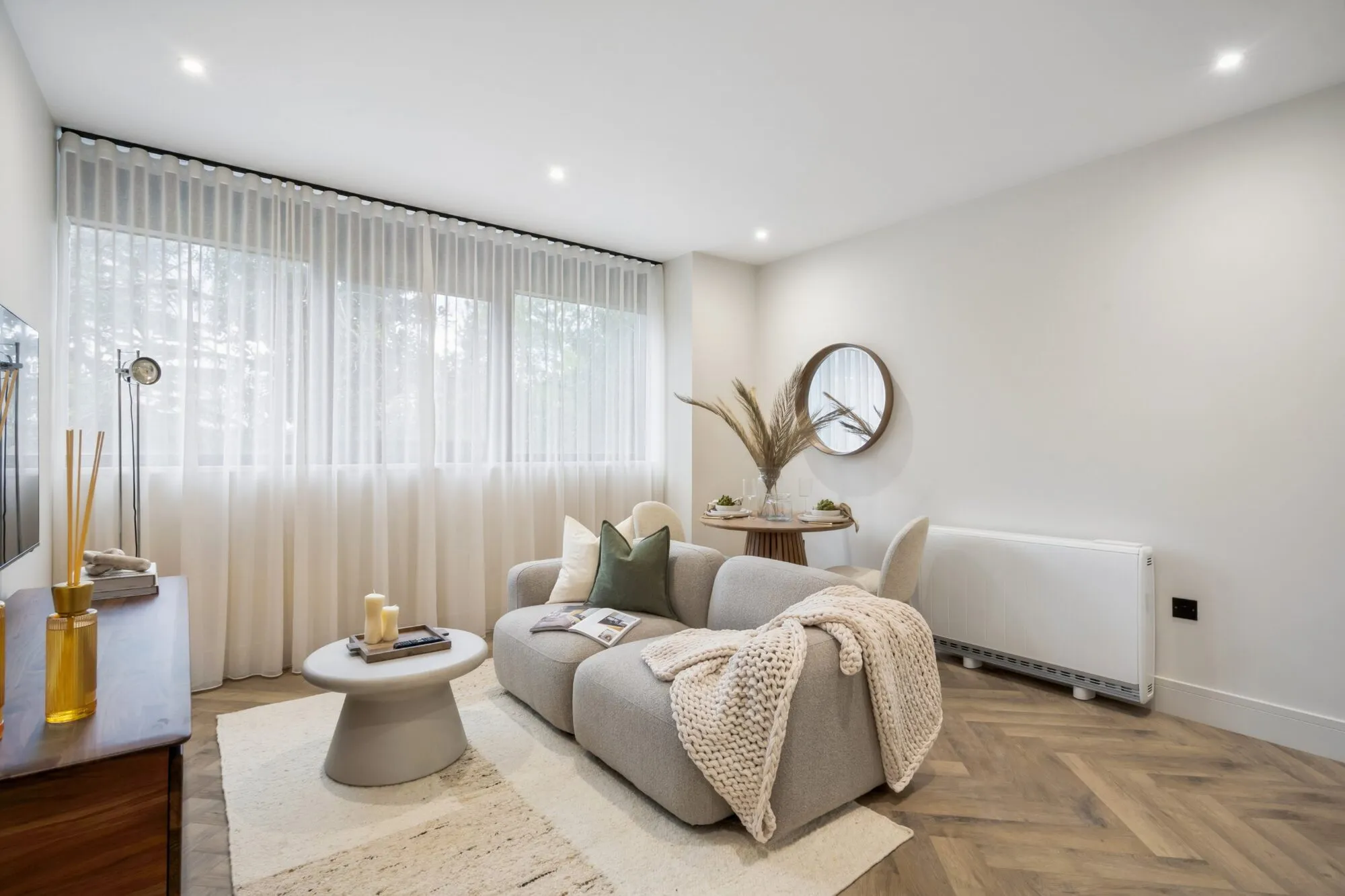 Living space in the show apartment, with a sofa, round dining table and full-height sheer curtains.
